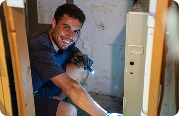 standard heating & air employee working on furnace unit smiling into camera