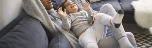 Woman on a couch playing with a child having fun with pillows on the couch.