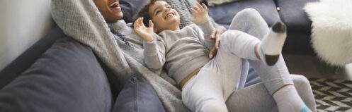 Woman on a couch playing with a child having fun with pillows on the couch.