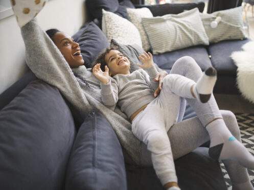 Woman on a couch playing with a child having fun with pillows on the couch.